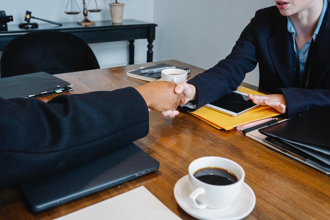 Diverse anonymous colleagues shaking hands at table with coffee and folders