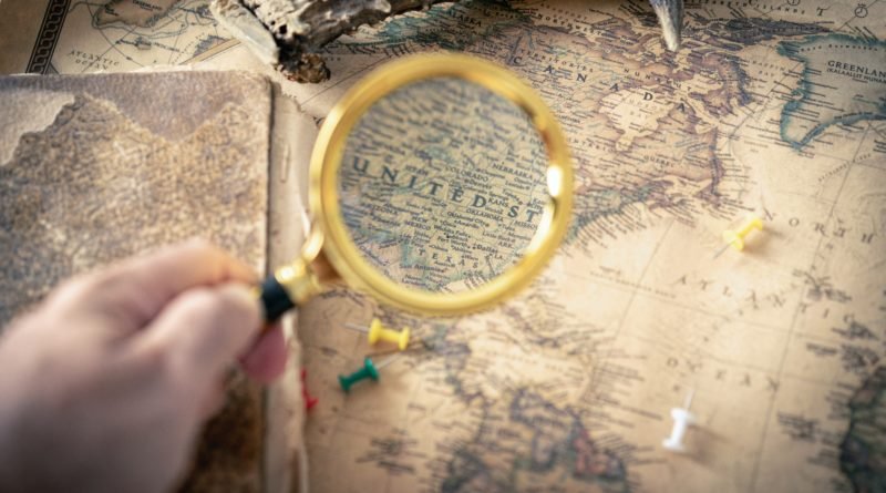 An image of a person's hand holding a magnifying glass, examining a map with various symbols and markings, representing the exploration and understanding of different types of illegal trades.